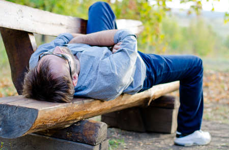 Young man stretched out on a wooden bench, relaxingの写真素材