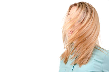 Head and shoulders portrait of a blonde woman with the wind in her hair blowing across and obscuring her face isolated on white with copyspaceの写真素材