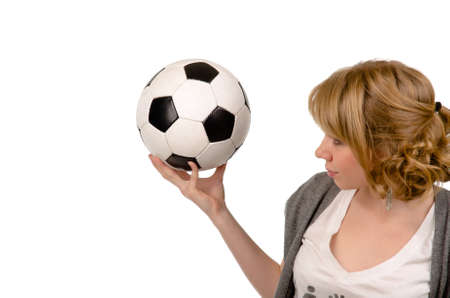Attractive young blonde woman holding up a black and white soccer ball or football in her hand isolated on white with copyspaceの写真素材