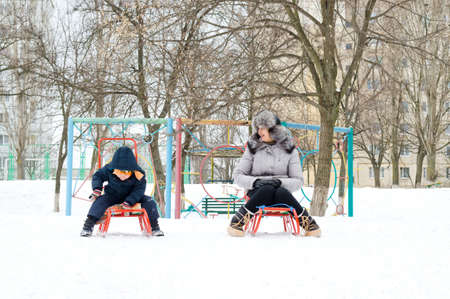 Attractive young mother and her small son bundled up against the cold weather sledding in a winter playground sitting astride their sleds in the snowの写真素材