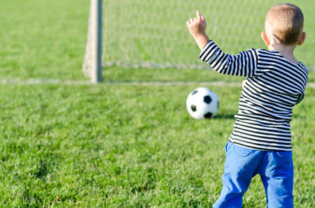 Rear view of a young boy kicking a soccer ball aiming at the goalposts and raising his hand to signal successの写真素材