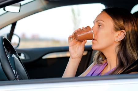 Woman driver sitting in a car stopping for a refreshing drink from a disposable takeaway cup before resuming her journeyの写真素材