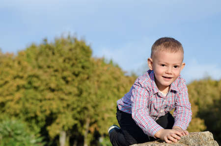 Happy little boy exploring outdoors clambering over a rock with a beautiful smile on his face with copyspaceの写真素材