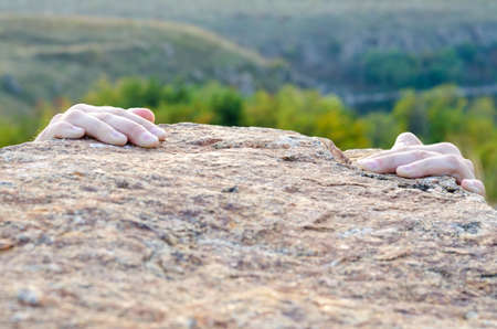 Male climber gripping a rocky ledge with just his fingertips in view on the granite against a valley backdropの写真素材