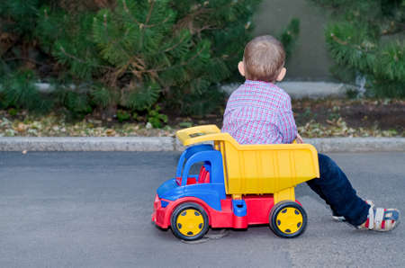 Little boy playing with a colourful plastic toy truck sitting on the back facing away from the cameraの写真素材