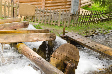 Flowing river water rushing from a sluice onto a small wooden waterwheelの写真素材