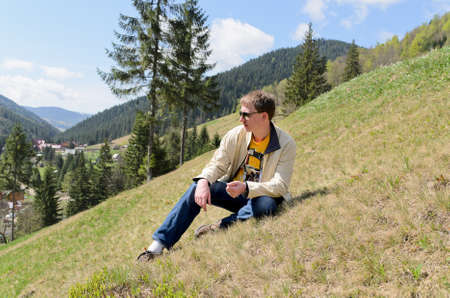 Casual young man wearing sunglasses sitting on a steep mountain slopeの写真素材