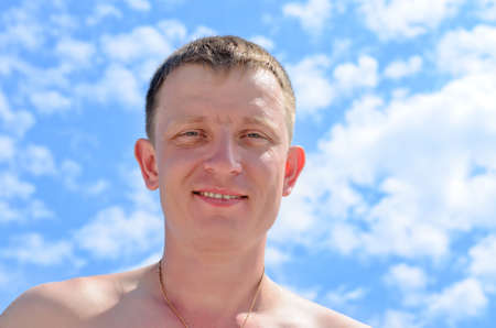 Portrait of a smiling blond young man against a blue sky with cloudsの写真素材