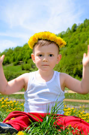 Cheerful young boy raising his hands and sitting on flower fieldの写真素材