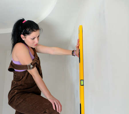 Woman finding a straight line with a spirit level holding iagainst wall in the vertical position...
