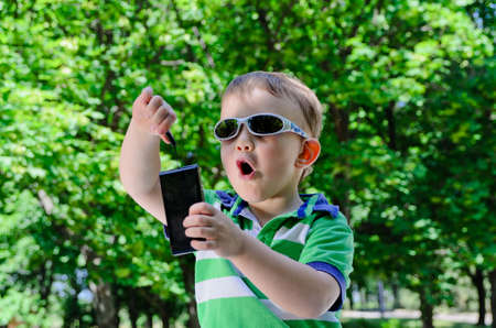 Amazed young child wearing sunglasses and playing with camera outdoorsの写真素材