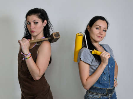 Two competent female interior decorators posing with a mallet and paint roller over their shoulders...