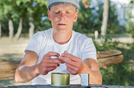 Man rolling his cigarettes concentrating on sealing the ground tobacco inside the paper as he sits at a rural wooden tableの写真素材