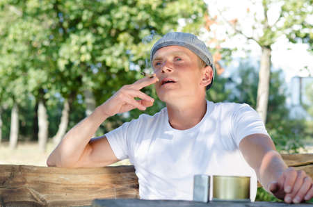 Low angle view of a good looking man sitting outdoors smoking at a rustic wooden tableの写真素材