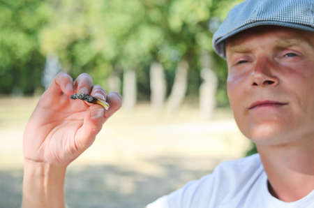 Close up cropped view of a casual trendy man sitting thinking outdoors in a park with a self rolled cigarette clasped between his fingersの写真素材
