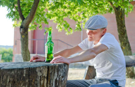 Man enjoying a quiet drink outdoors sitting at a rustic wooden table in the garden with a large bottle of alcohol in front of himの写真素材