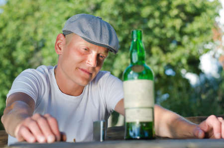 Portrait of a depressed middle-aged man sitting at the table in the garden looking at a bottle of white wineの写真素材