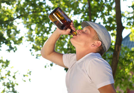 Jobless depressed middle-aged Caucasian man drinking alcohol from a bottle, in the park