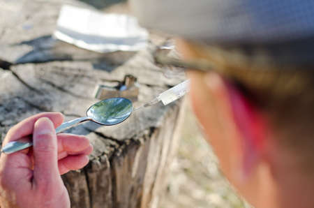 Rear view of the close-up of an addicted man preparing a dose with focus on the soluble heroin heated in a teaspoonの写真素材