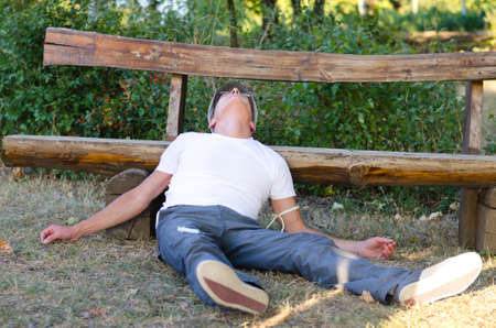 Middle-aged man lying down on the ground leaning his head on a bench feeling sick because of drug...