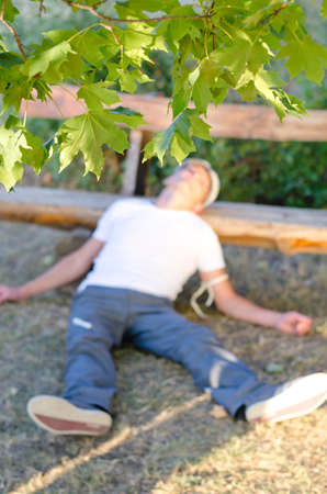 Addicted Caucasian middle-aged man lying down on the ground leaning his head on a bench feeling sick because of drug abuseの写真素材