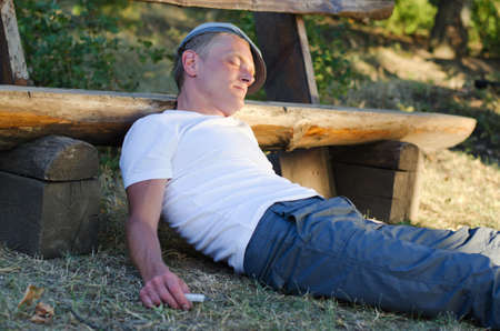 Drug addict with a syringe in his hand lying sprawled on the ground oblivious to his surroundings as he experiences the high of a drug like cocaineの写真素材