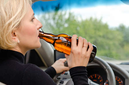 Close up view from behind of a woman alcoholic drinking from a bottle of alcohol as she drives the...