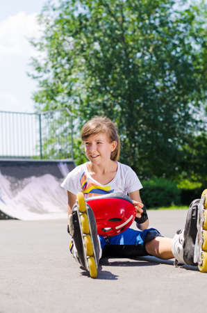 Young roller skater enjoying her summer vacation sitting on the asphalt in the hot summer sunshine relaxing in her roller blades and skating gearの写真素材