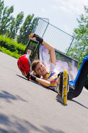 Pretty young teenage girl out rollerblading taking a fall lying on her back on the tarmac with her arms outflungの写真素材