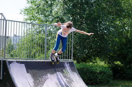 Active energetic young teenage girl roller blading launching herself from the top of a cement ramp...