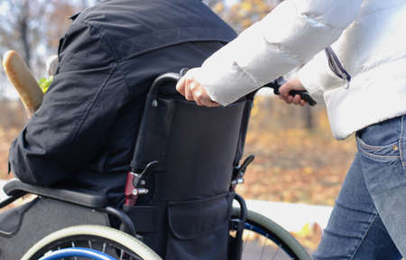 Close up view of the hands of a woman pushing a disabled man in a wheelchair along a rural street in...