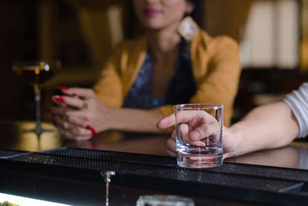 Man with an empty glass at the bar signalling to the barman with his finger for a refill, selective...