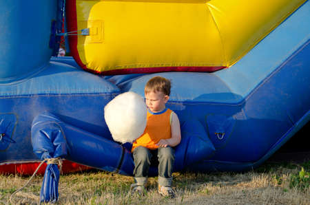 Cute small boy enjoying a stick of candy floss eating it while sitting on a plastic jumping castle...