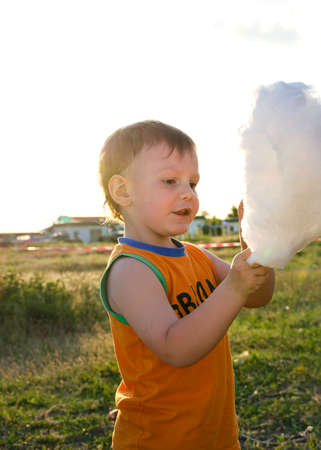 Adorable little boy standing outdoors in the countryside enjoying a stick of cotton candy or candy floss plucking at it with his hand while smiling with pleasure at the treatの写真素材