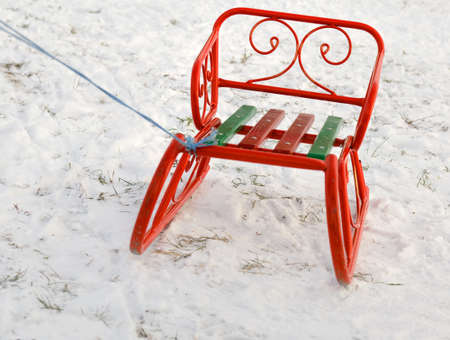 Ornate orange toboggan or sled standing in fresh white winter snow with a rope attached so that a young child can pull it up the slopeの写真素材