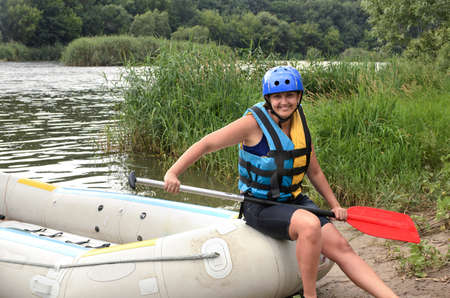 Woman going white water rafting sitting in a helmet and life jacket on an inflatable raft holding a paddle at the side of a riverの写真素材