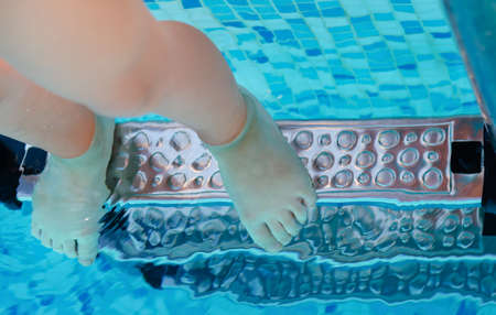 Bare feet of a young child underwater standing on the top rungs of a set of swimming pool stepsの写真素材