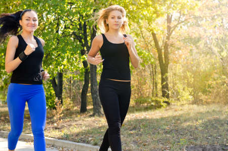 Two attractive young female friends jogging together in a park doing an early morning training workoutの写真素材