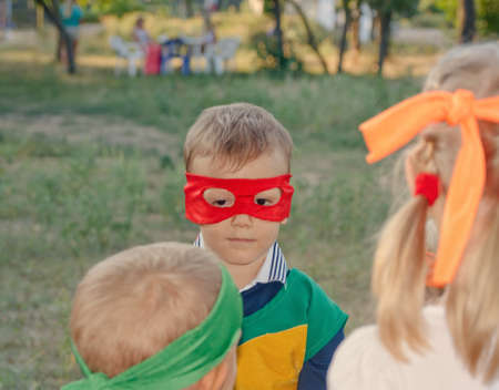 Young boy playing at a kids birthday party wearing a super hero mask as he chats to his young friendsの写真素材
