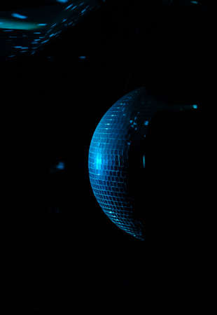Colorful turquoise blue mirrored metallic disco ball in a nightclub hanging in the darkness with...
