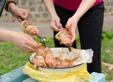 Closeup of the hands of a young woman preparing kebabs to grill on a BBQ threading spicy meat and onions from a basin onto metal skewersの写真素材