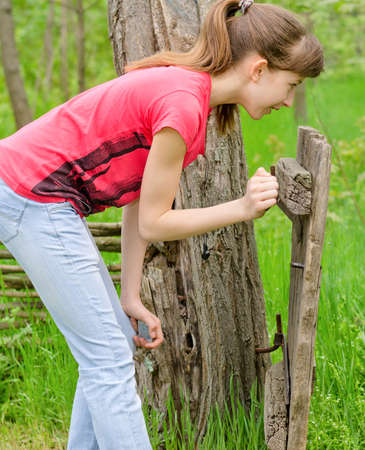 Attractive young teenage girl standing behind an old dilapidated wooden gate watchingの写真素材