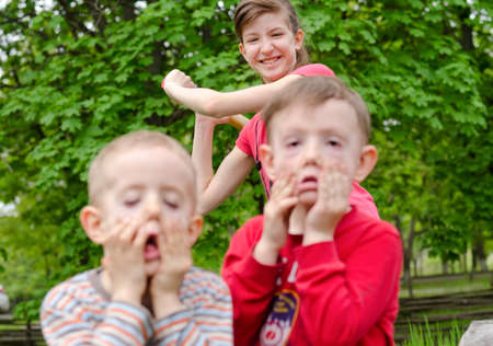 Two young boys pulling faces watched by a pretty teenage girl with an amused smile on her face standing behind them, focus to the smiling teenagerの写真素材