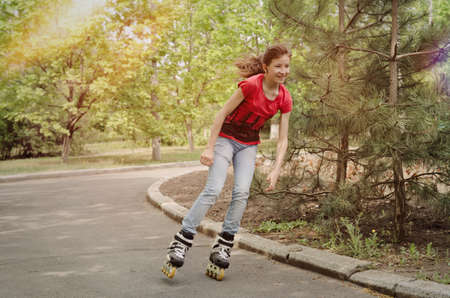 Beautiful young teenage girl roller skating cornering at speed on a tarred rural road with her ponytail flying out behind herの写真素材