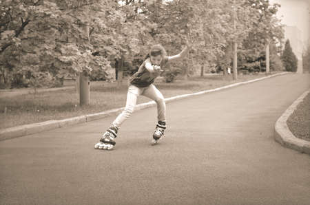 Beautiful young teenage girl roller skating cornering at speed on a tarred rural road with her ponytail flying out behind herの写真素材