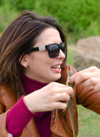 Laughing beautiful young woman wearing sunglasses standing holding a lizard in her hands alongside a rural laneの写真素材