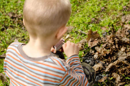 Child striking a safety match on a box of matches against a green grass background , close up of the...
