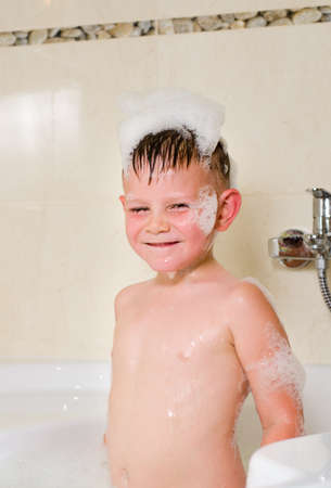 Cute boy with bubbles on his head in the bathtub