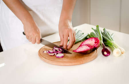 Housewife standing at a counter in the kitchen chopping fresh vegetables and onions to be added as ingredients to her recipeの写真素材