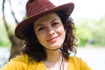 Beautiful woman in a trendy leather cowboy style brown hat smiling at the camera with a lovely smile as she enjoys a day in the countrysideの写真素材